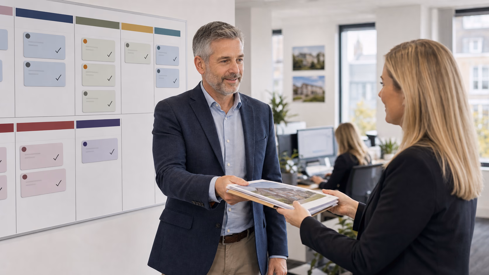 A senior estate agent handing a property file to a colleague while a wall board shows sales and lettings stages in an Irish agency office