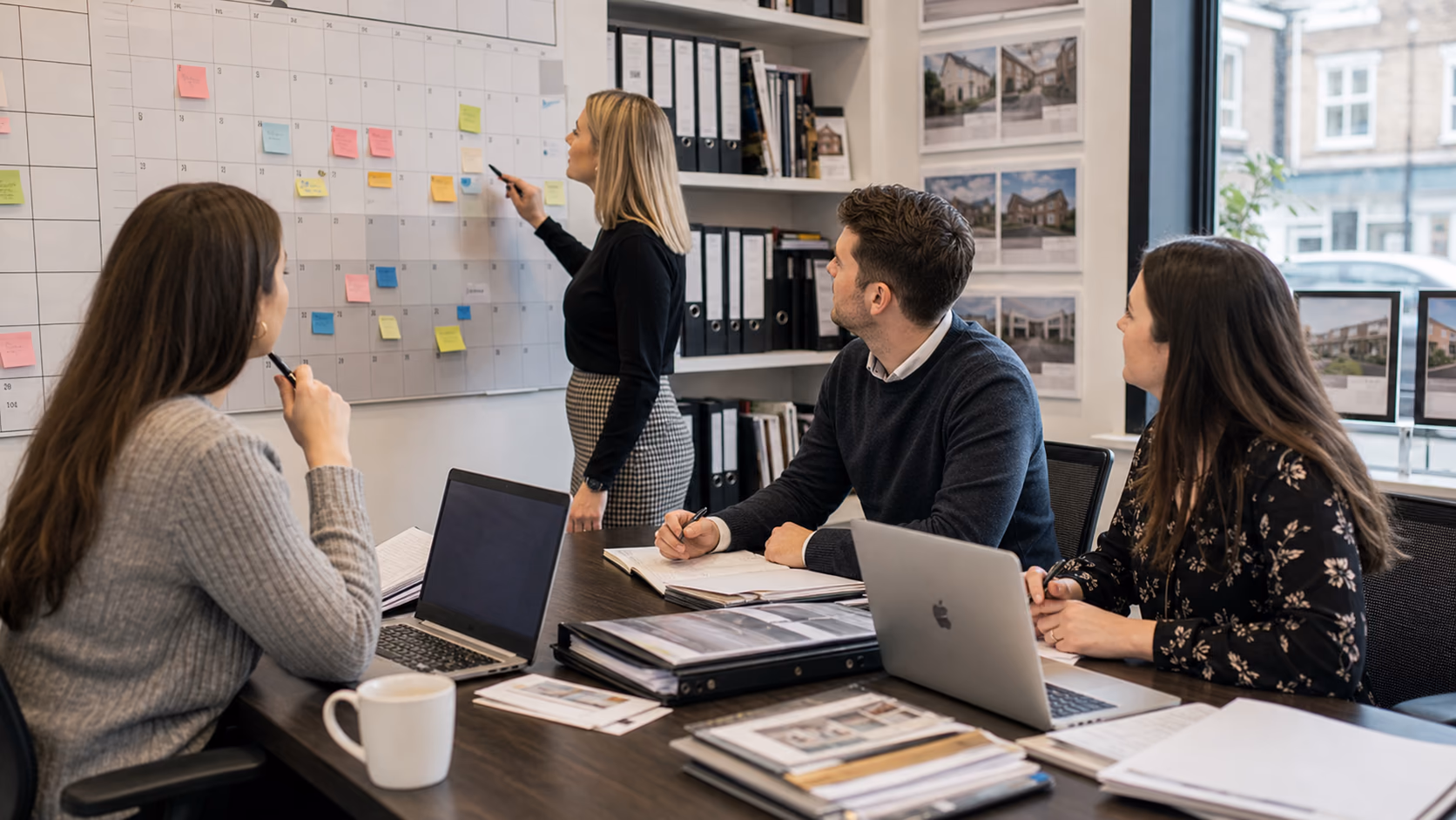 A letting agency team discussing renewal dates and maintenance tasks on a wall calendar beside property folders and laptops