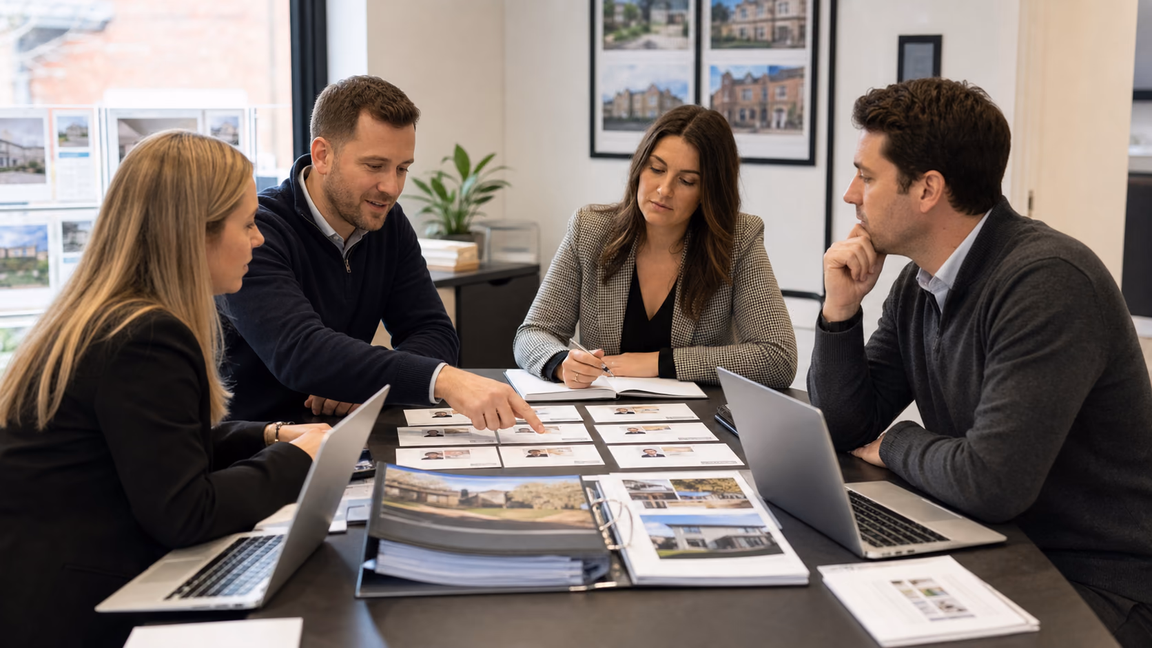 A regional estate agency team reviewing client role cards on a meeting table with branch notes and property files beside laptops